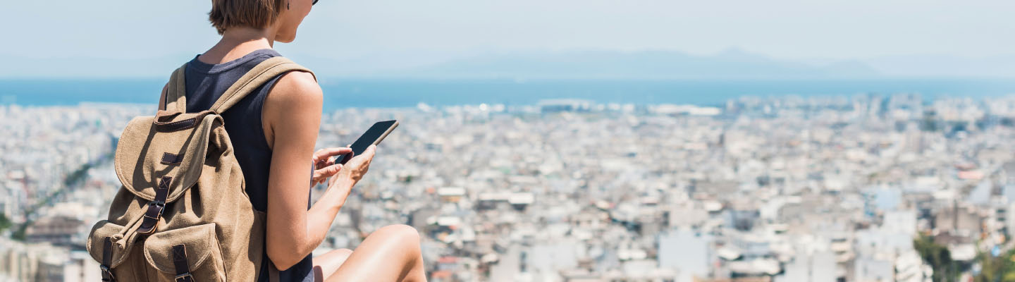 Woman outdoors overlooking city while looking down at a cell phone