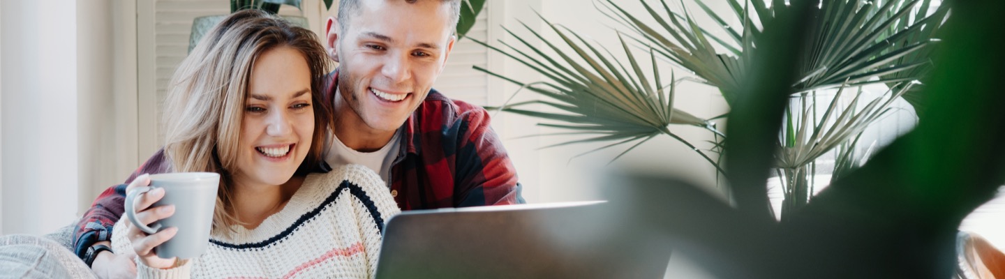 Young couple with laptop on couch near plant